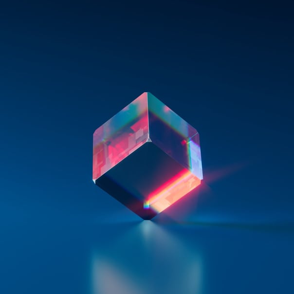 Picture of a transparent cube with red and blue colors standing on a glass floor on one of its corners. There is a reflection on this cube on the glass floor.